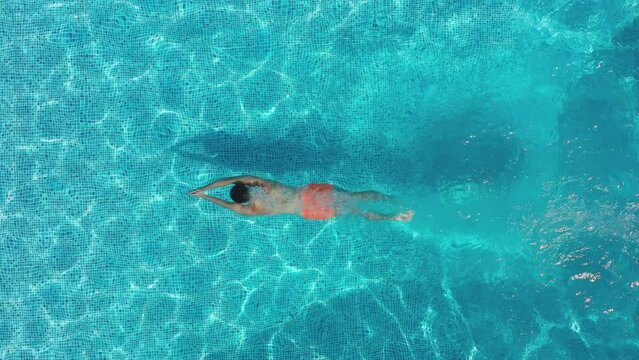 Overhead drone shot of man diving into outdoor pool and swimming underwater - shot in slow motion