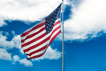 Large American flag waving in the wind against a cloudy blue sky.