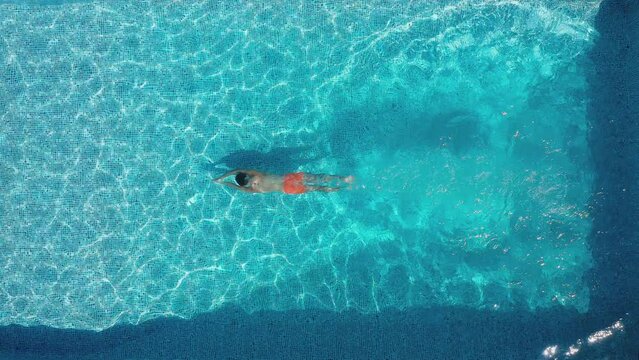 Overhead drone shot of man diving into outdoor pool and swimming underwater - shot in slow motion