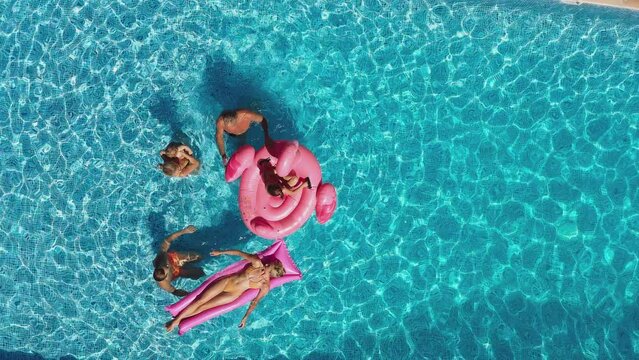 Overhead drone shot of multi-generation family with baby boy on summer holiday relaxing on inflatables and splashing in swimming pool - shot in slow motion