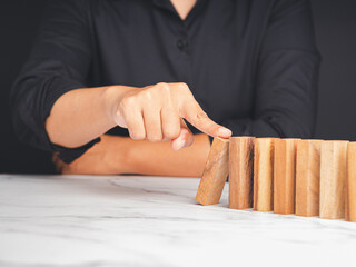 Hand of a businesswoman pushing a wooden block on a line of dominos while sitting in the office