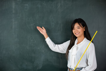 Back to school concept. Happy beautiful young woman standing hold pointer to back board, Asian female teacher smiling with wooden stick pointing to blackboard at school in classroom, Education