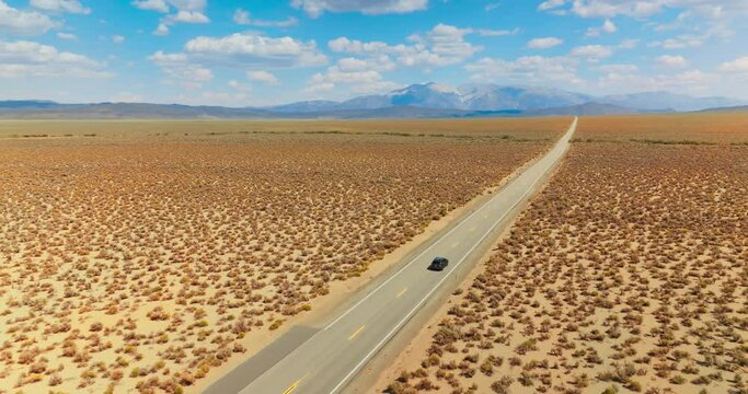 Following the black cars riding by the empty road through the deserted land. Highway from California to Nevada footage on sunny day. Mountain at backdrop.