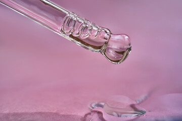Dropper with serum or cosmetic oil on a pink background.