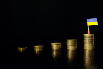 Ukraine economic growth, recovery after financial crisis and currency appreciation concept. Ukrainian flag in increasing stack of coins in dark black background.