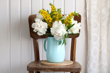 A bouquet of white peonies and yellow verbena in a blue enameled jug.