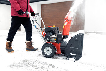 Detail closeup of portable red snow blower powered by gasoline in action. Senior mature man outdoor...