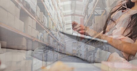 Fototapeta na wymiar Caucasian woman using laptop shopping online over a warehouse full of boxes 