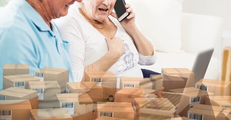 Caucasian senior couple using laptop shopping online with a pile of boxes 