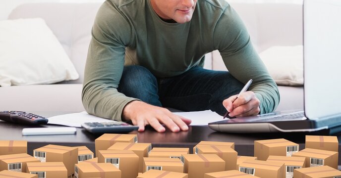 Caucasian man using laptop shopping online with a pile of boxes 