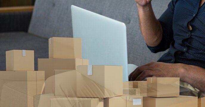 Caucasian man using laptop shopping online with a pile of boxes 