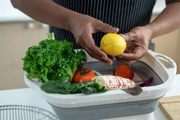 Male senior hands washing lemon and vegetables for making fresh salads in the kitchen, healthy food