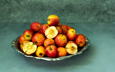Ripe red small Ranetka apples on a metal plate, on a gray or blue background.