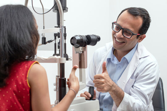 Indian girl and optometrist doing eye test with slit lamp in modern ophthalmology clinic, checking retina of a girl eye, ophthalmologist thumbs up child girl
