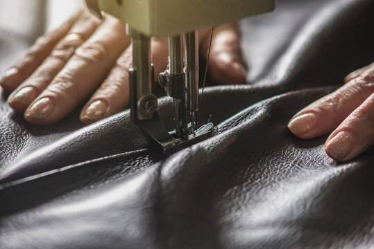 Women's hands in the process of sewing on professional equipment. Sewing leather in production. Close-up