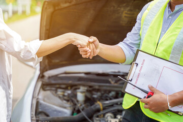 Closeup and crop of a congratulatory handshake of insurance employee and customer with sun flare on car engine background.