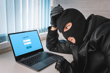 A thief in a balaclava mask is thinking about a password to log in. The concept of identity theft.. Hacker With Log On Screen, Computer Fraud Concept Background