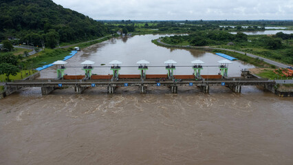 Fototapeta premium Aerial view of the water released from the concrete dam's drainage channel as the overflow in the rainy season. Top view of turbid brown forest water flows from a dam in rural northern Thailand.