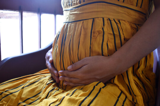 Six months pregnant woman sitting and touching belly near the window closeup