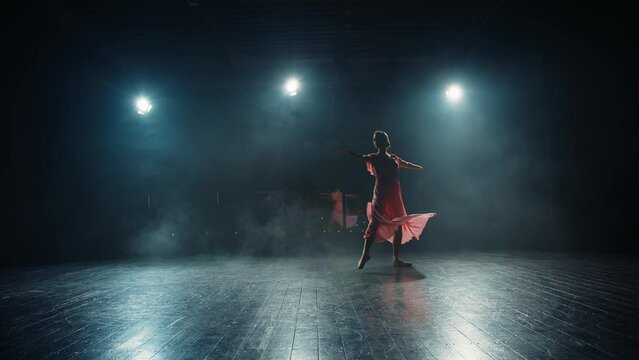 Silhouette of ballerina dancing on stage. Young woman ballet dancer is spinning in flowing dress ine backlight of spotlights