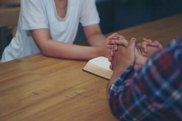 group of asian catholic pray, hope for peace the world and free from war and coronavirus. Young man and woman Hand in hand together on bible (worship christian), thinking and closed eyes at church