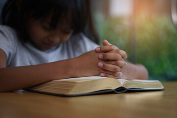 Prayer and bible concept. Asian kid praying, hope for peace and free from war and coronavirus, Hand in hand together by child. Little Girl believes and faith in christian religion at church.