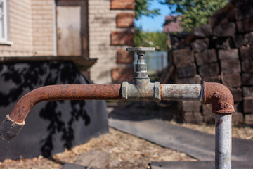 Rusty faucet for water supply. In the courtyard of an abandoned village house there is an old non-working water column. There is no water in the system due to a shutdown. Selective focus.