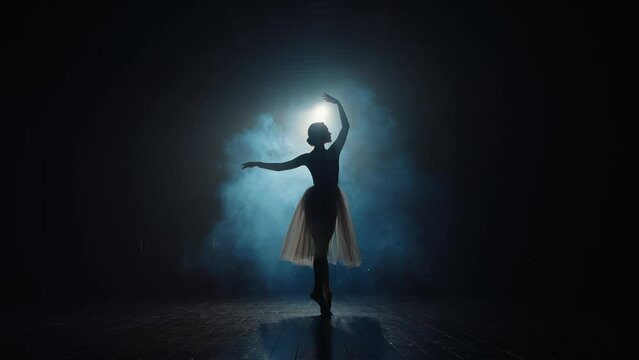 Silhouette of ballerina in backlight of spotlights. Graceful ballet dancer spins on toes in pointe shoes