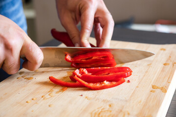 man hands cutting red pepper close up on wooden board