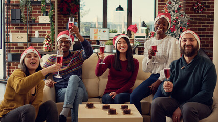 Portrait of festive coworkers clinking glasses with alcohol to celebrate christmas holiday time with toast or cheers. People celebrating winter festivity event with wine beverage in decorated office.