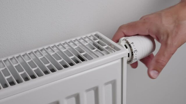Man adjusting temperature on heating radiator, Energy crisis concept in Europe, Rising costs in private households for gas bill due to inflation and war