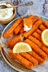 Close up of   Crispy breaded  deep fried fish fingers with breadcrumbs served  with remoulade sauce and  lemon Cod Fish Nuggets on rustic wood table background