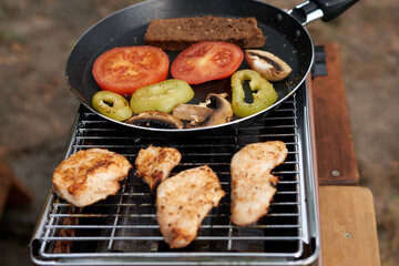 Cooking on a gas grill in nature. Chicken meat and roasted vegetables in a pan. 