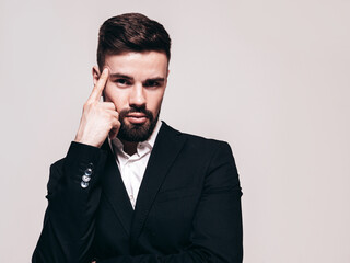 Portrait of handsome confident stylish hipster lambersexual model. Sexy modern man dressed in elegant black suit. Fashion male posing in studio near white wall. Isolated on grey