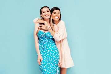 Two young beautiful smiling brunette hipster female in trendy summer dresses. Sexy carefree women posing near blue wall. Positive models having fun. Cheerful and happy. Isolated