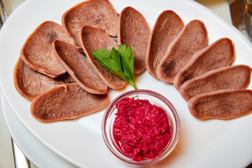 Cutted Beef tongue with horseradish and herbs on a white plate