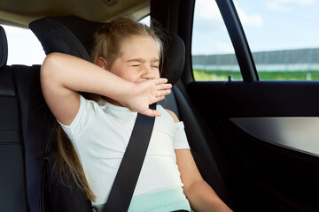 Caucasian little girl yawning while riding in car