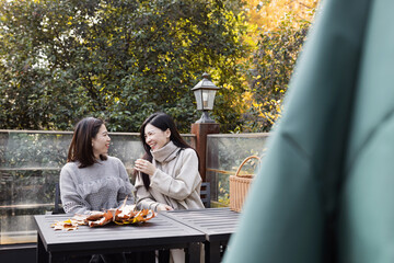 Asian girlfriends having fun together with maple leaves outdoor. Friendship concept with happy...