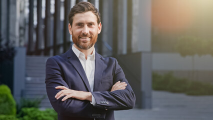 Successful confident smiling businessman in suit stands outdoors on background office building...