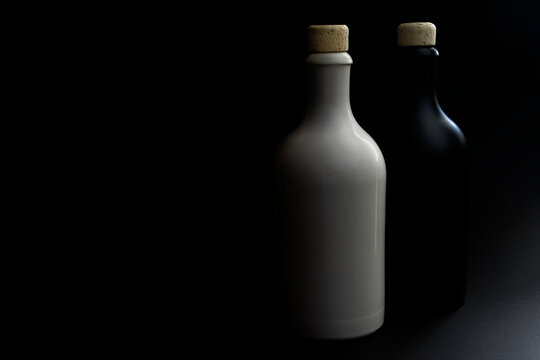 Two ceramic gin bottles in white and black with natural cork against black background. The photo was taken with low light. The bottles are placed in the right third. Copy space for your design.