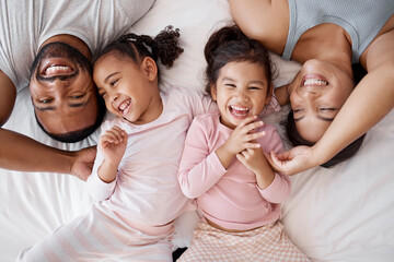 Happy family, love and morning tickling with parents and children lying and playing in bedroom for fun together at home from above. Laughing and man and woman spending time with playful kids to bond