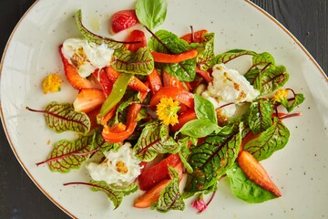 Vegetarian salad with strawberries, bell peppers, Basil and mozzarella, dressed with olive oil in a white plate on a white background.