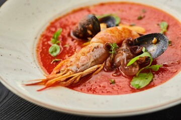 Tomato soup with seafood, shrimp, octopus, mussels and other shellfish for cooking dinner on a black background. Healthy food handmade