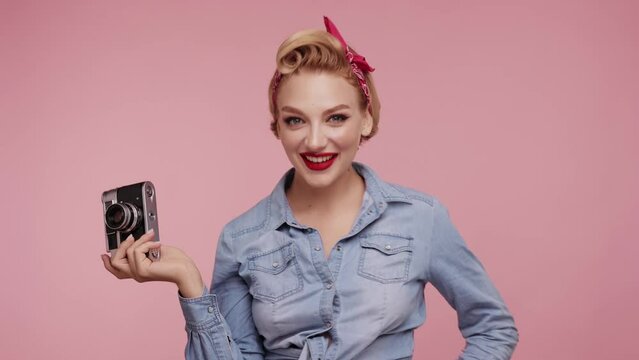 Cute woman in denim jacket isolated on pink color background in studio Look at the camera, holds camera and simulates taking a picture. Pretty Pin-up blond Girl. Retro, pin-up style.