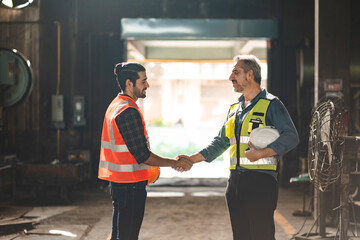 Caucasian factory engineer talking and shaking hands on business cooperation agreement. Successful hand shaking after good deal, workers handshaking each other at heavy industrial production line.