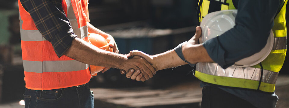 Caucasian factory engineer talking and shaking hands on business cooperation agreement. Successful hand shaking after good deal, workers handshaking each other at heavy industrial production line.