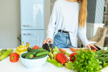 Woman lay out fresh vegetables and greens on table in stylish kitchen. Housewife make salad for dinner. Organic products without nitrates. Vegetarianism, proper nutrition, healthy eating, cooking.