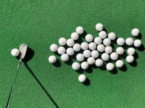 Group of practice golf balls on practice artificial grass mat with one club iron address at one ball under morning sunlight. - Powered by Adobe