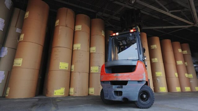 A forklift is carrying paper at the factory. The forklift is carrying a large roll of paper. Loader at the wallpaper factory