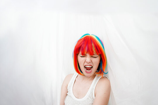 Woman with colorful dyed hair screaming by plastic backdrop